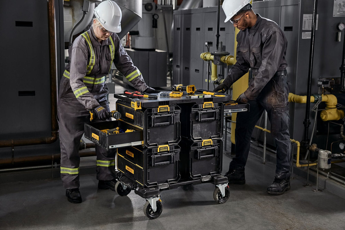 Industrial workspace scene with two workers using a large DEWALT ToughSystem rolling tool storage cart featuring multiple drawers organized DEWALT tools and heavy duty construction.