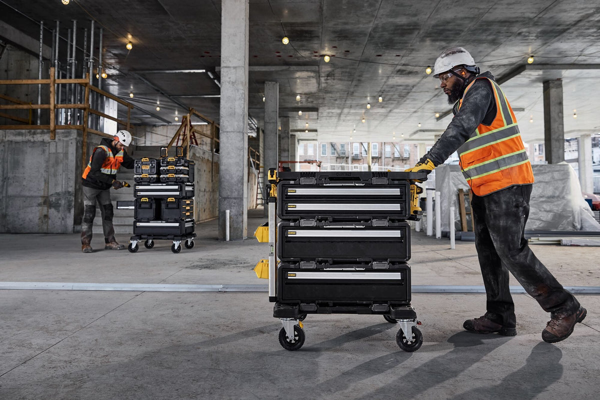 Construction site with worker pushing a DEWALT ToughSystem rolling tool chest featuring multiple drawers modular stacking capability and rugged mobility for jobsite tool organization.
