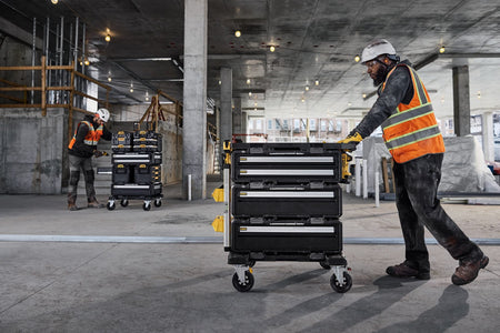 Construction site with worker pushing a DEWALT ToughSystem rolling tool chest featuring multiple drawers modular stacking capability and rugged mobility for jobsite tool organization.