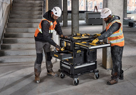 Two construction workers beside a DEWALT ToughSystem mobile tool cart loaded with power tools and accessories demonstrating organized tool management on an active jobsite.