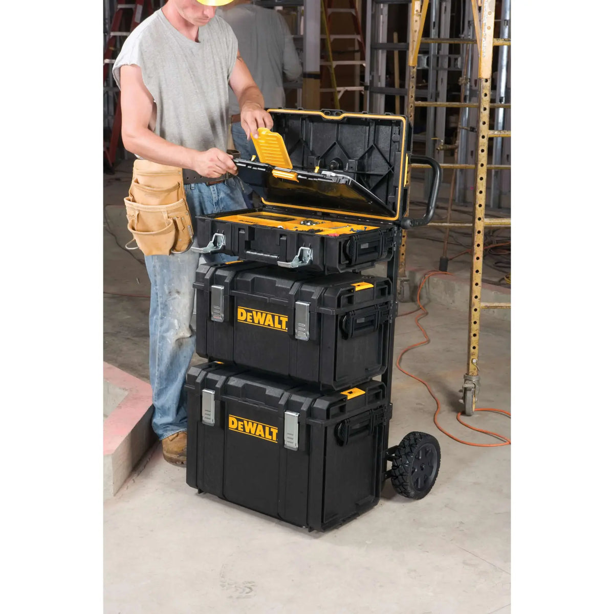 A lifestyle shot of a professional contractor using the DEWALT DS Carrier on a jobsite. The cart is shown carrying a full stack of three ToughSystem tool boxes, demonstrating how the adjustable brackets provide access to specific tools without unstacking the entire unit.