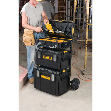 A lifestyle shot of a professional contractor using the DEWALT DS Carrier on a jobsite. The cart is shown carrying a full stack of three ToughSystem tool boxes, demonstrating how the adjustable brackets provide access to specific tools without unstacking the entire unit.