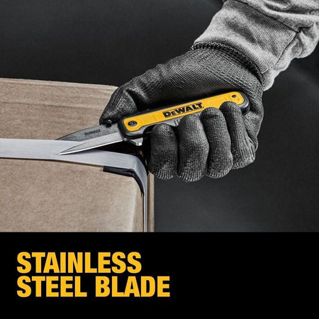 Gloved hand using DEWALT DWHT10993 utility knife with stainless steel blade to cut plastic strap on cardboard box; bold text highlights blade material.