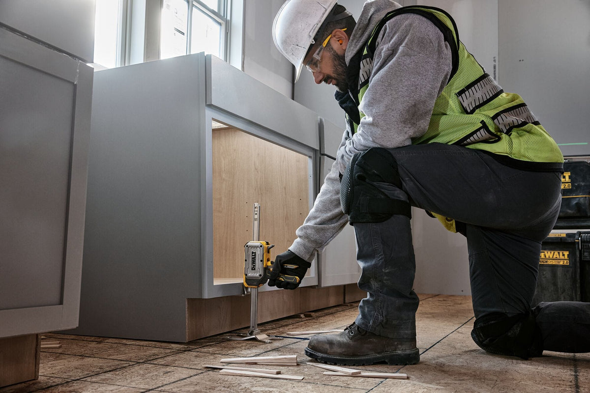 Contractor using DeWalt DWHT83550 construction jack slim base to lift base cabinet for accurate shimming and leveling.