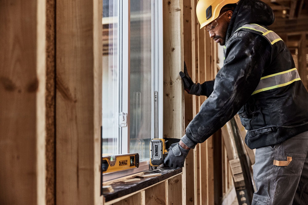 Worker adjusting window frame alignment with a DeWalt DWHT83550 construction jack resting on rough framing sill.