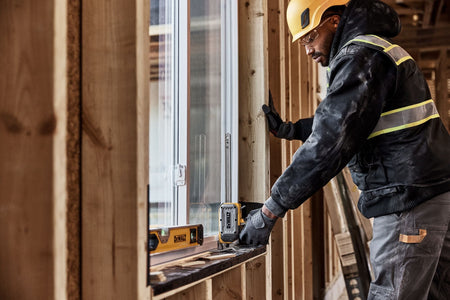 Worker adjusting window frame alignment with a DeWalt DWHT83550 construction jack resting on rough framing sill.