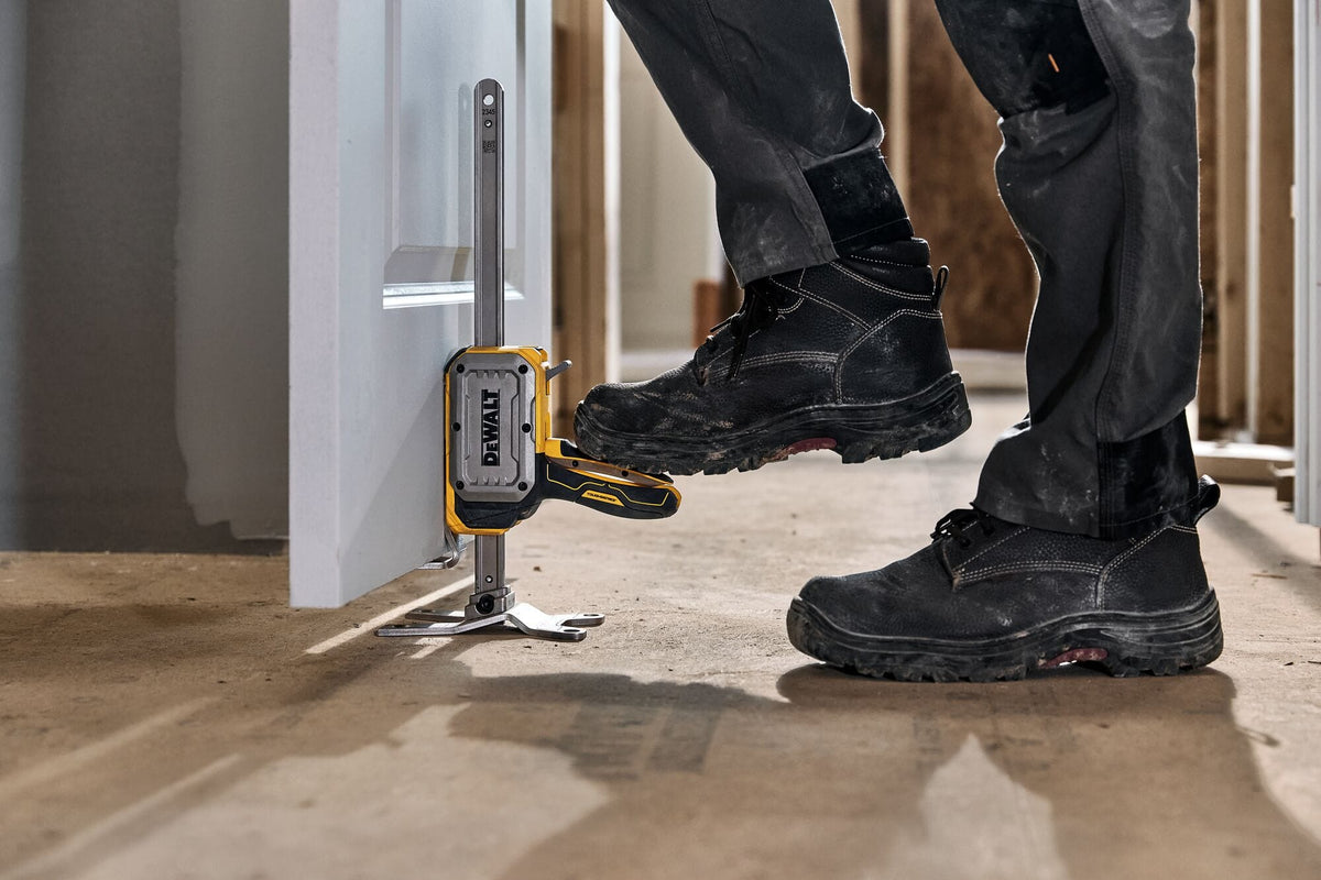 Hands-free step-to-lift pedal on DeWalt DWHT83550 jack elevated by work boot to align a heavy solid door.
