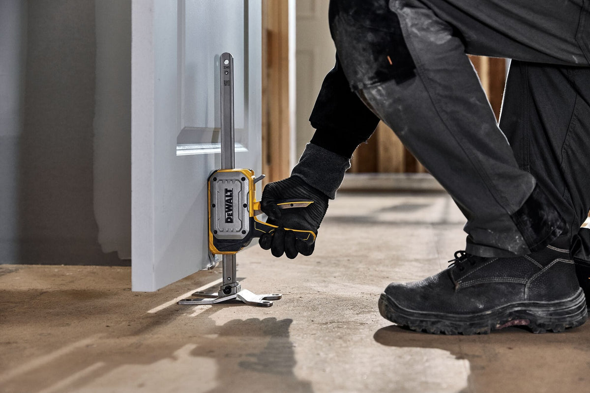 Operator squeezing trigger grip of DeWalt DWHT83550 construction jack to lift heavy door off subfloor for hinge installation.