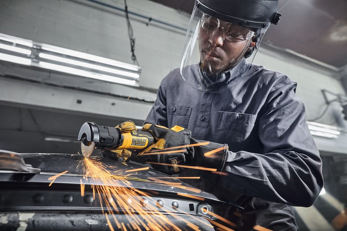 Action on-site view identical to image twelve, showing a metalworker holding the compact DeWalt 20V MAX brushless cordless 3-inch cut-off tool over structural automotive components, generating a stream of bright friction sparks, as a product performance visualization example