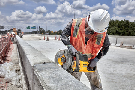 Worker scoring highway concrete using the DeWalt 9-inch cut-off saw with water feed to suppress silica dust.