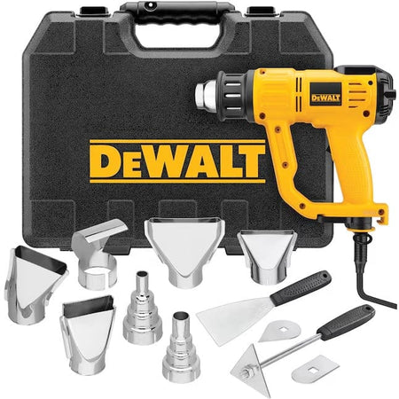 Studio view of the complete DeWalt heat gun kit, showing the black hard carrying case standing behind the yellow tool and an assortment of silver metal nozzles and scraper blades arranged in the foreground.