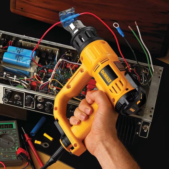 Close-up of a technician using the heat gun with a reflector nozzle attachment to shrink tubing on electrical wires during an electronics repair.