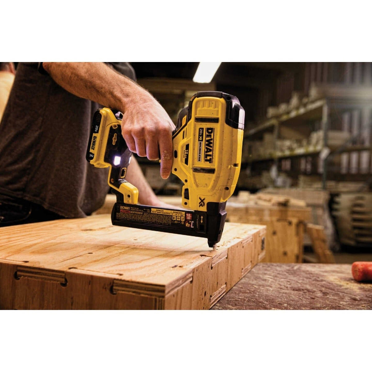 An action shot of a worker using the DeWalt DCN681 cordless stapler to fasten a piece of plywood.