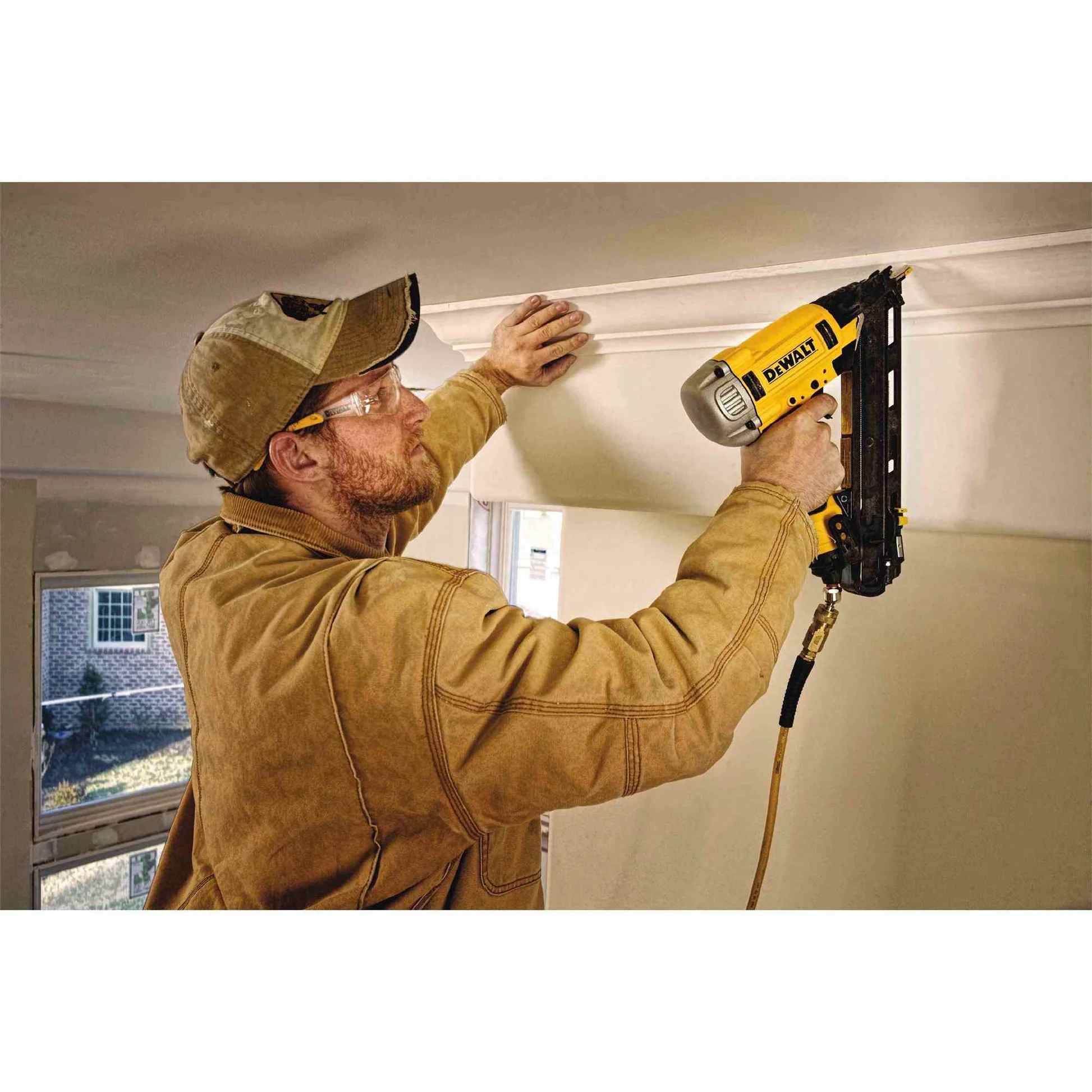 An action shot of a worker in safety glasses using the DeWalt DWFP72155 finish nailer to install white crown molding on a ceiling.