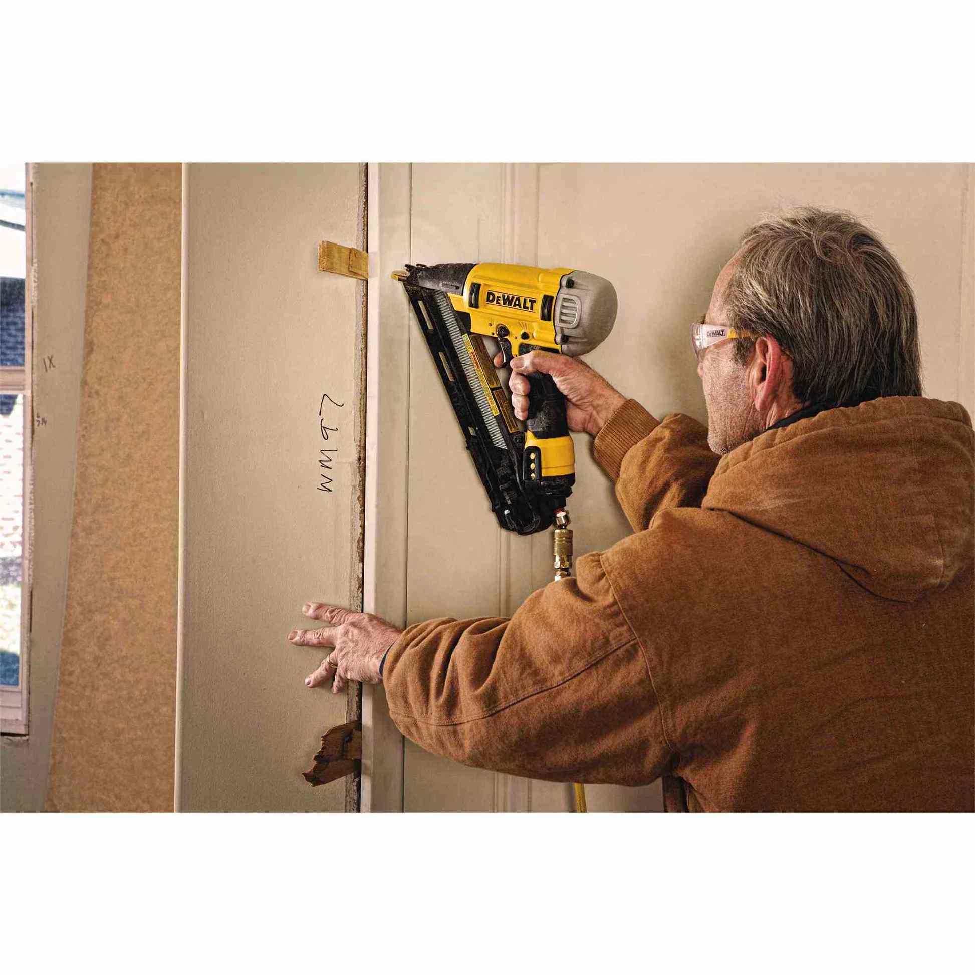 An action shot of a worker using the DeWalt DWFP72155 angled finish nailer to install wooden door trim.