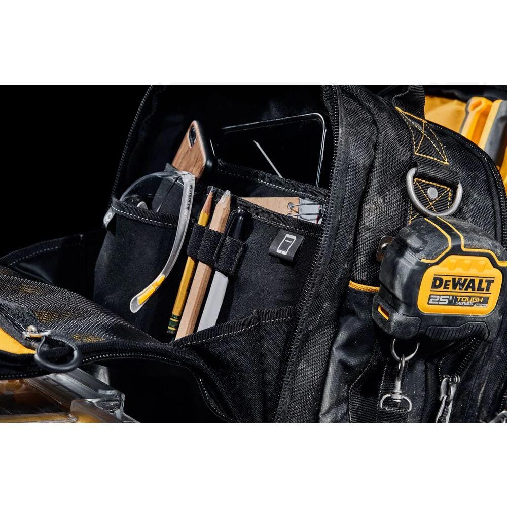 Close-up view of the open tool bag interior filled with jobsite gear, showing a tablet stored in a protected back sleeve, safety glasses, pencils, and a marker in dedicated slots, plus a DeWalt tape measure clipped to the exterior side.