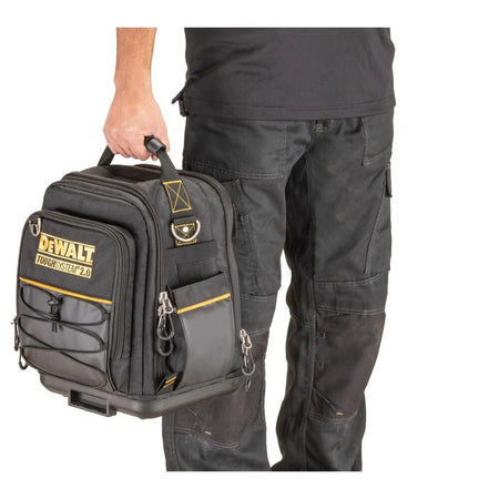 A worker holding the DeWalt compact tool bag down at their side by its rugged top carrying handle, demonstrating the manual transport grip and the bag's scale relative to a person.