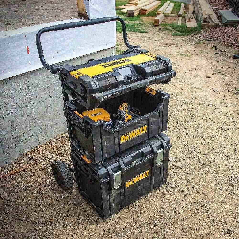 The DeWalt tote utilized in a full modular storage stack on a trolley, positioned securely between a large bottom toolbox and a top-mounted ToughSystem radio, holding cordless drills for quick access.