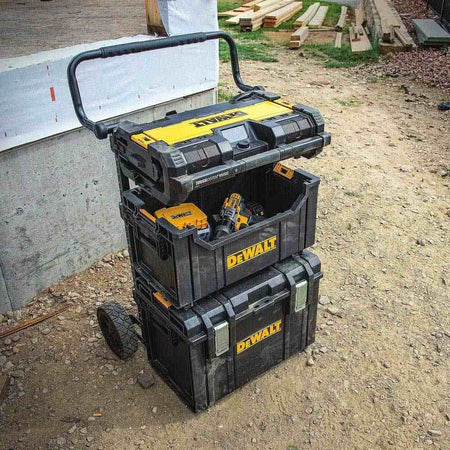 The DeWalt tote utilized in a full modular storage stack on a trolley, positioned securely between a large bottom toolbox and a top-mounted ToughSystem radio, holding cordless drills for quick access.