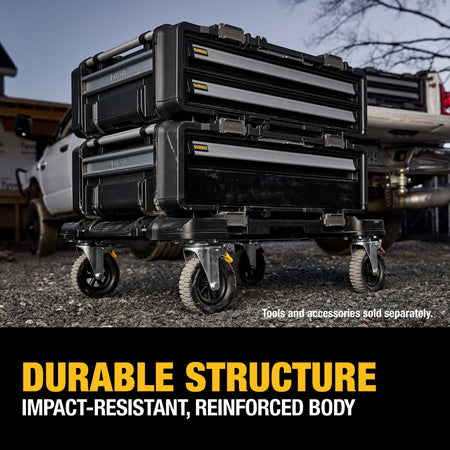An outdoor jobsite application photo displaying two DEWALT ToughSystem 2.0 DXL drawer units stacked and locked together on top of a black four-wheeled rolling dolly trolley over a gravel ground workspace, with a pickup truck in the background and a lower text callout reading DURABLE STRUCTURE IMPACT-RESISTANT, REINFORCED BODY.