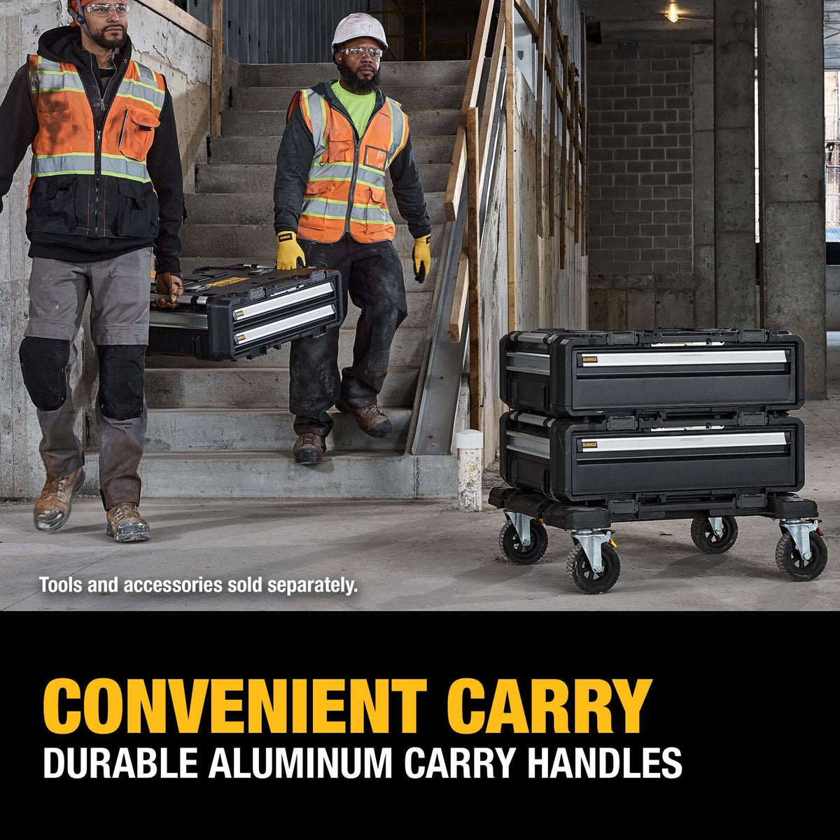An indoor jobsite application lifestyle photo of two construction tradesmen wearing white hard hats and safety vests carrying a DEWALT modular drawer box unit down a concrete staircase at a commercial construction building site, while a separate stacked cart assembly stands on the floor, complete with lower text reading CONVENIENT CARRY DURABLE ALUMINUM CARRY HANDLES.
