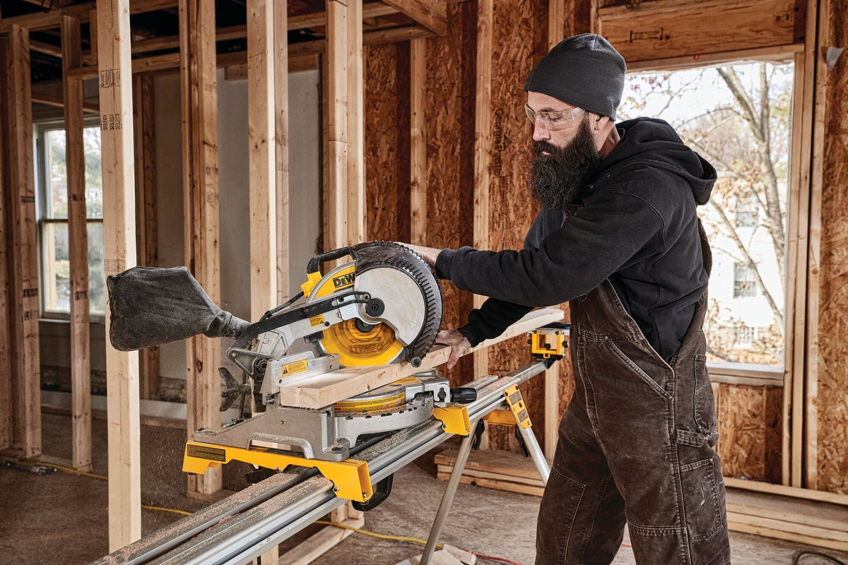 Carpenter making a crosscut on dimensional lumber using the DeWalt DWS713 10-inch miter saw mounted on a portable jobsite stand.