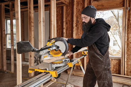 Carpenter making a crosscut on dimensional lumber using the DeWalt DWS713 10-inch miter saw mounted on a portable jobsite stand.