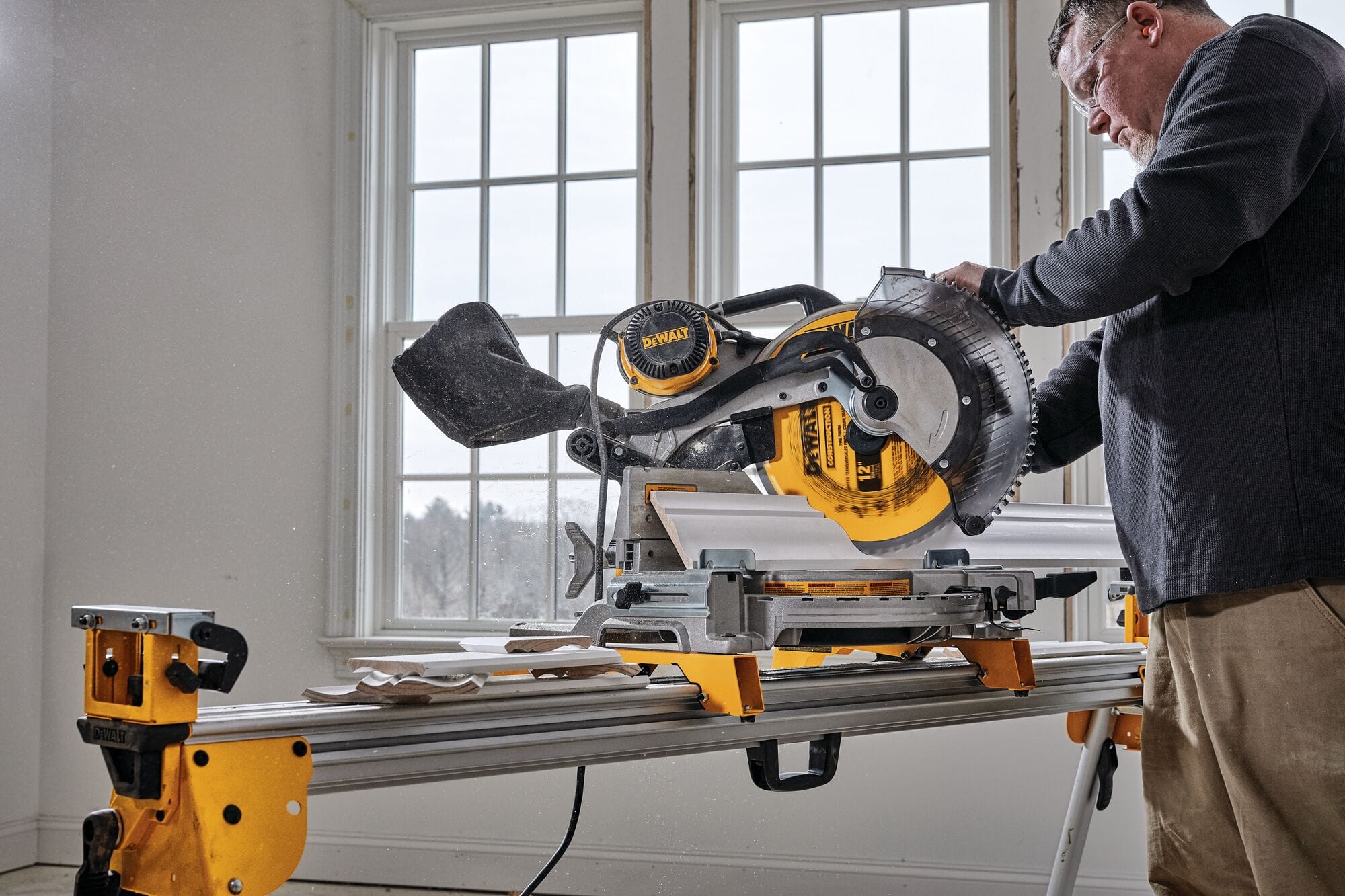 Finish carpenter cutting white crown molding vertically nested against the tall sliding fences of the DeWalt DWS716 miter saw.
