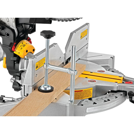 Vertical material clamp holding a hardwood board securely against the aluminum base fence on the DeWalt DWS716 miter saw.