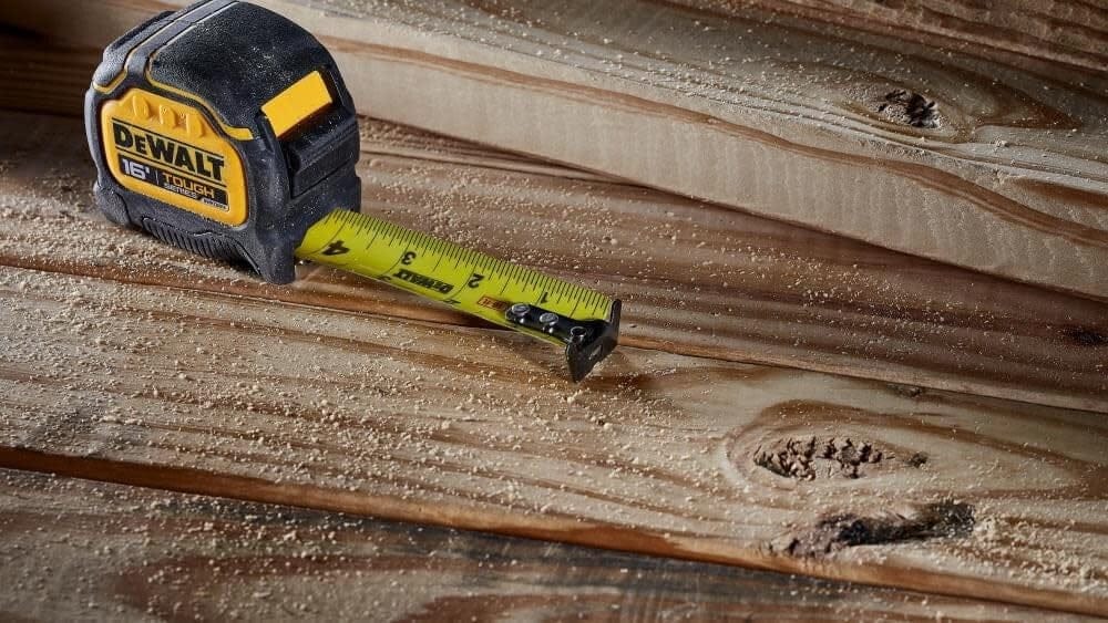 The DeWalt tape measure sitting on sawdust-covered wooden planks with the blade extended, demonstrating stability and durability in a construction environment.