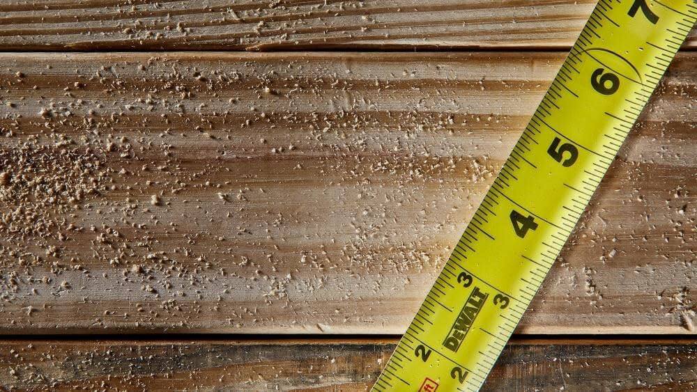 Overhead close-up view of the extended yellow tape blade resting on wood, showing the precise 1/16 inch graduation markings and DeWalt branding.