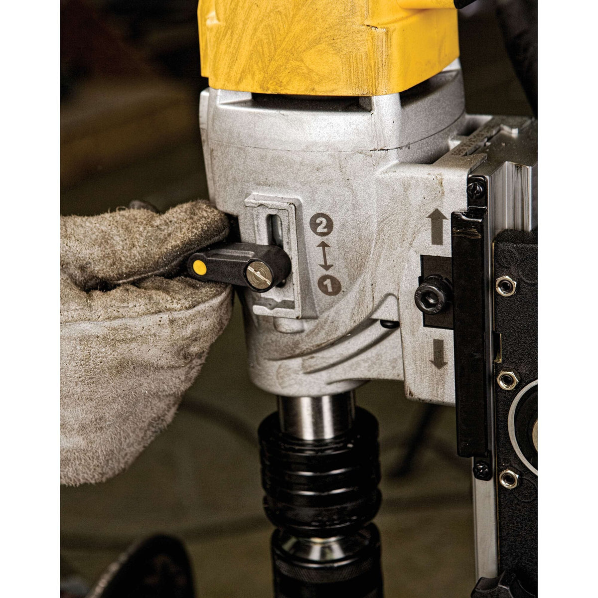 A close-up view of the mechanical gear selection switch on the side of the Dewalt magnetic drill press, showing a hand in a textured leather safety work glove shifting the black toggle lever between speed setting 1 and speed setting 2.