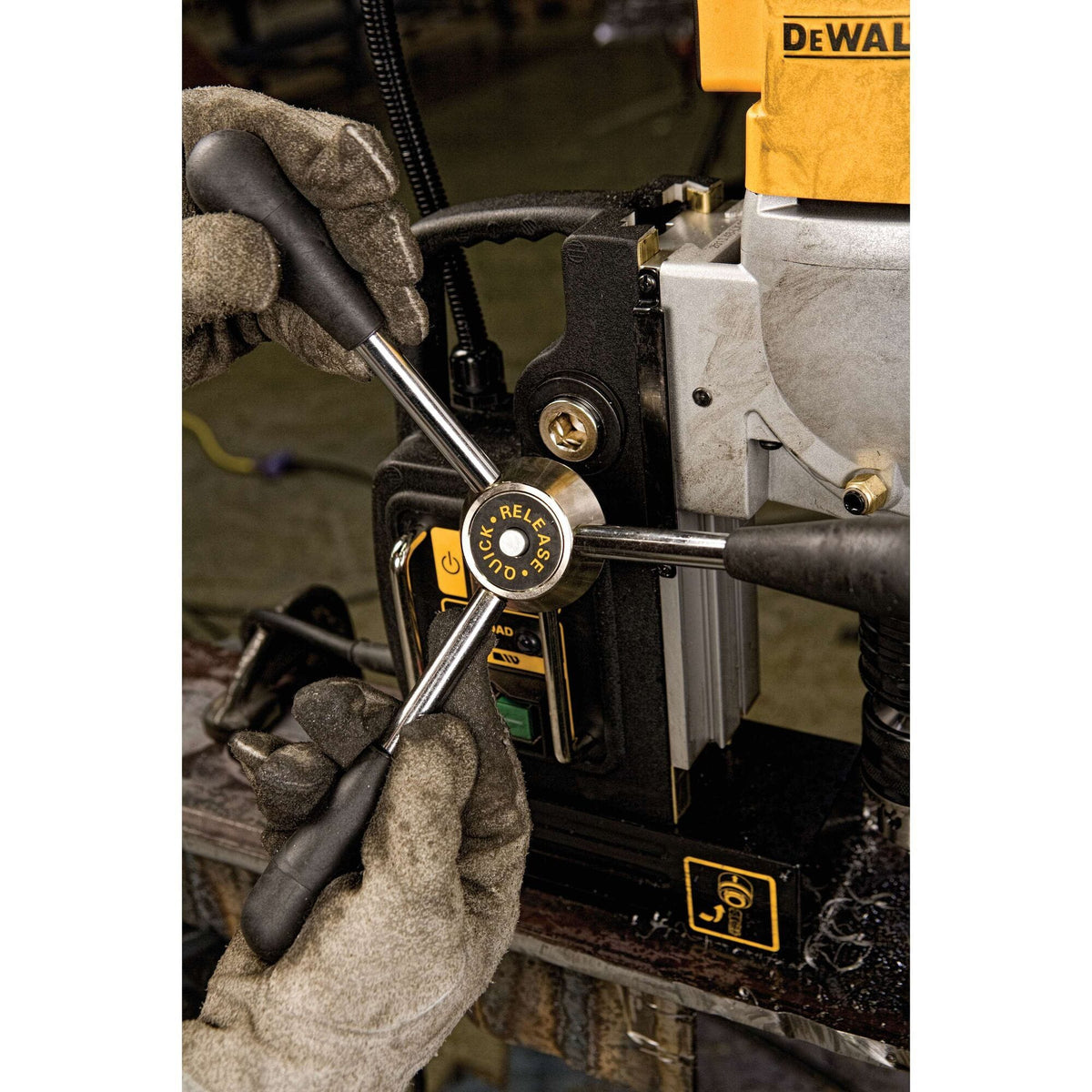 A detailed jobsite view showing a worker in thick leather safety gloves operating the quick-release three-spoke feed handle wheel of the yellow and black Dewalt magnetic drill press machine.