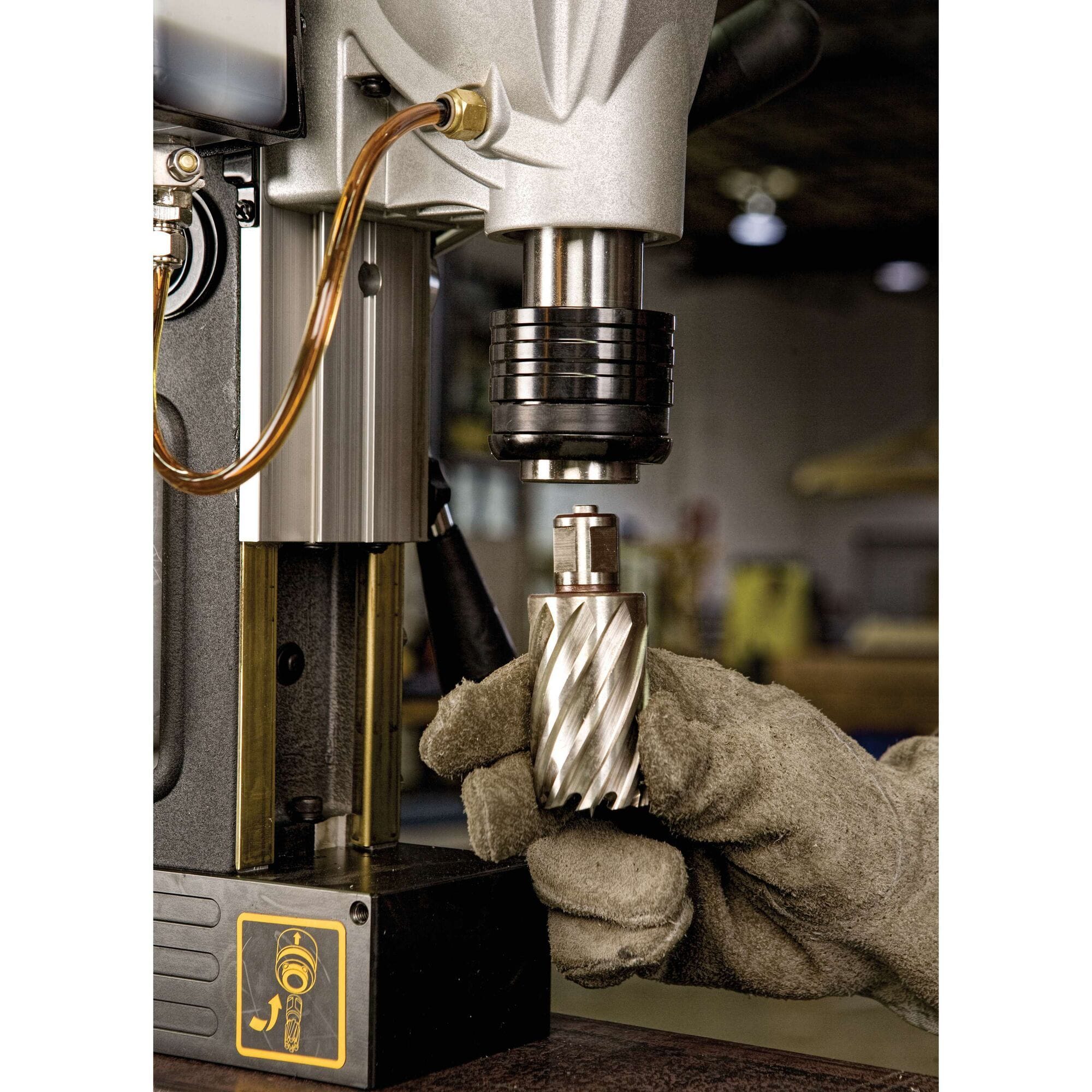 A macro photograph of a gloved hand inserting a steel annular core cutter bit up into the tool-free quick-change chuck mechanism of the portable Dewalt magnetic drill press.