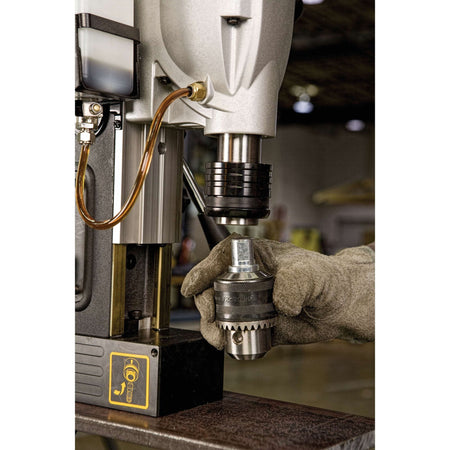 A close-up field photograph detailing a technician's gloved hand installing a heavy-duty 1/2-inch keyed chuck adapter into the toolless Weldon shank arbor of the portable steel drilling machine.