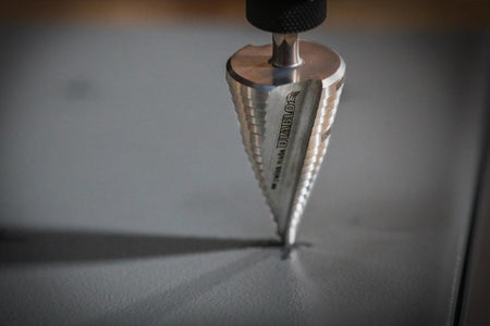 Close-up of a Diablo step drill bit actively drilling into a metal surface; conical shape and stepped design visible with emphasis on precision and durability.