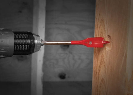 Action shot of a Diablo 1-3/8 -inch spade bit attached to a cordless drill boring a clean hole into a vertical wood stud on a construction site.