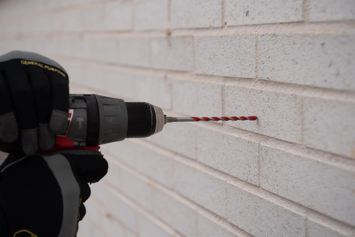 Action shot of a Diablo Red Granite hammer drill bit attached to a cordless drill while boring a precise hole into a white brick masonry wall.