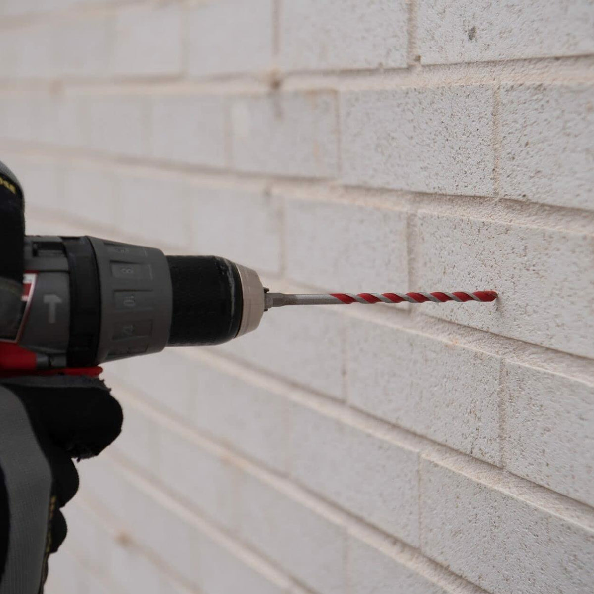 Close-up of a person using a cordless drill with a red Diablo bit to drill into a white brick wall, demonstrating masonry application and tool compatibility.