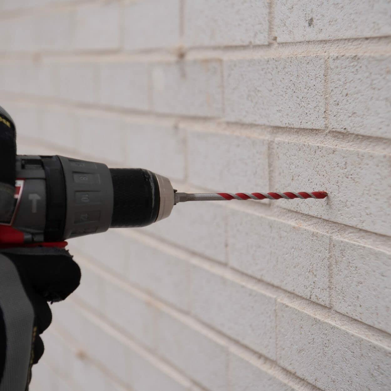 Close-up of a person using a cordless drill with a red Diablo bit to drill into a white brick wall, demonstrating masonry application and tool compatibility.