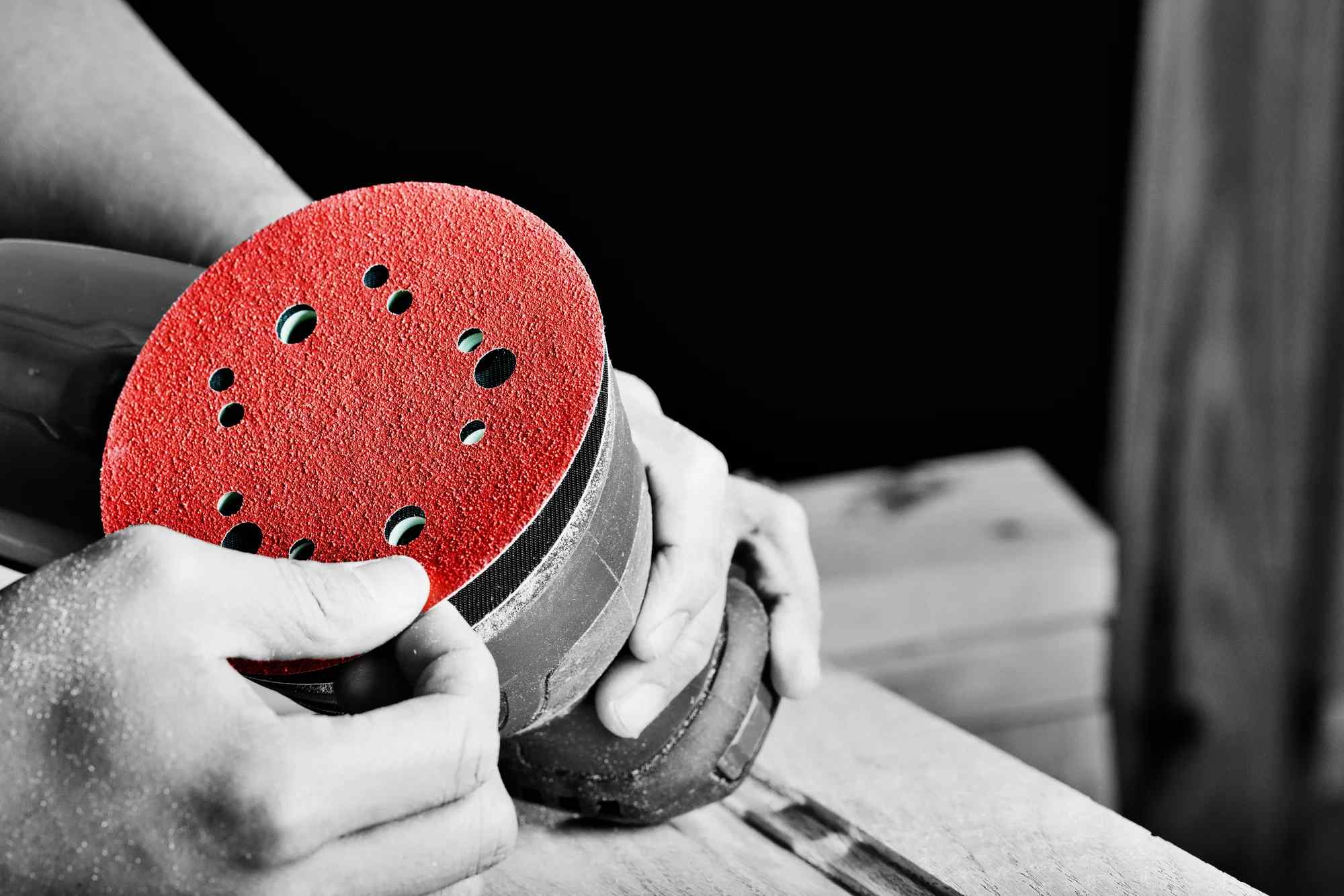 A close-up view of a professional's hands attaching a red Diablo 5 inch 180-grit Hook and Lock sanding disc to a random orbital sander in a woodworking shop.