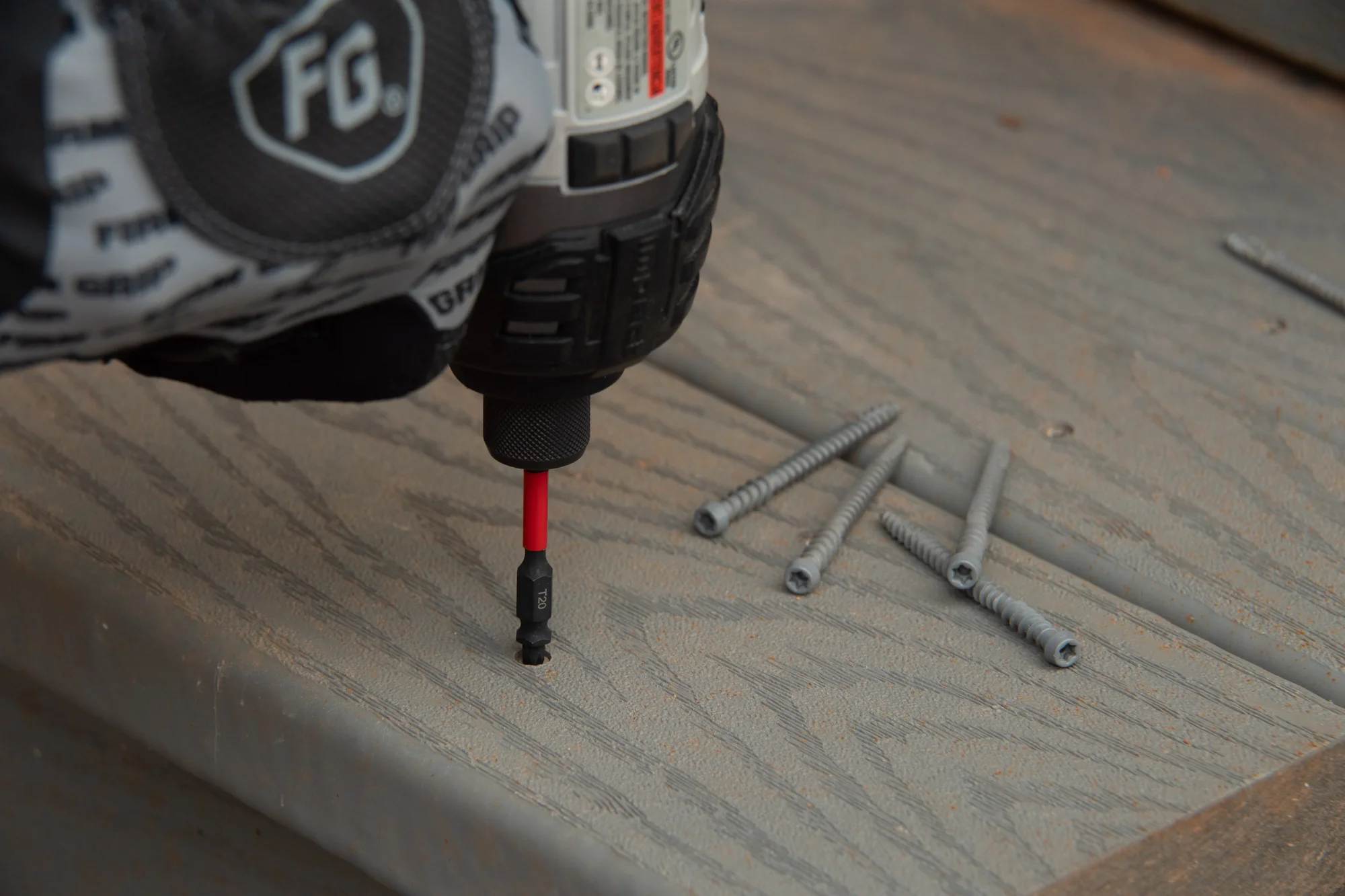 Close-up view of an impact driver sinking a screw into a grey composite deck board using a Diablo impact bit