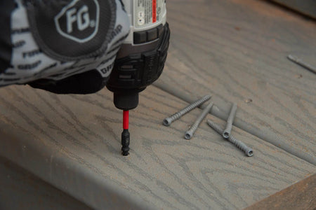 Close-up view of an impact driver sinking a screw into a grey composite deck board using a Diablo impact bit