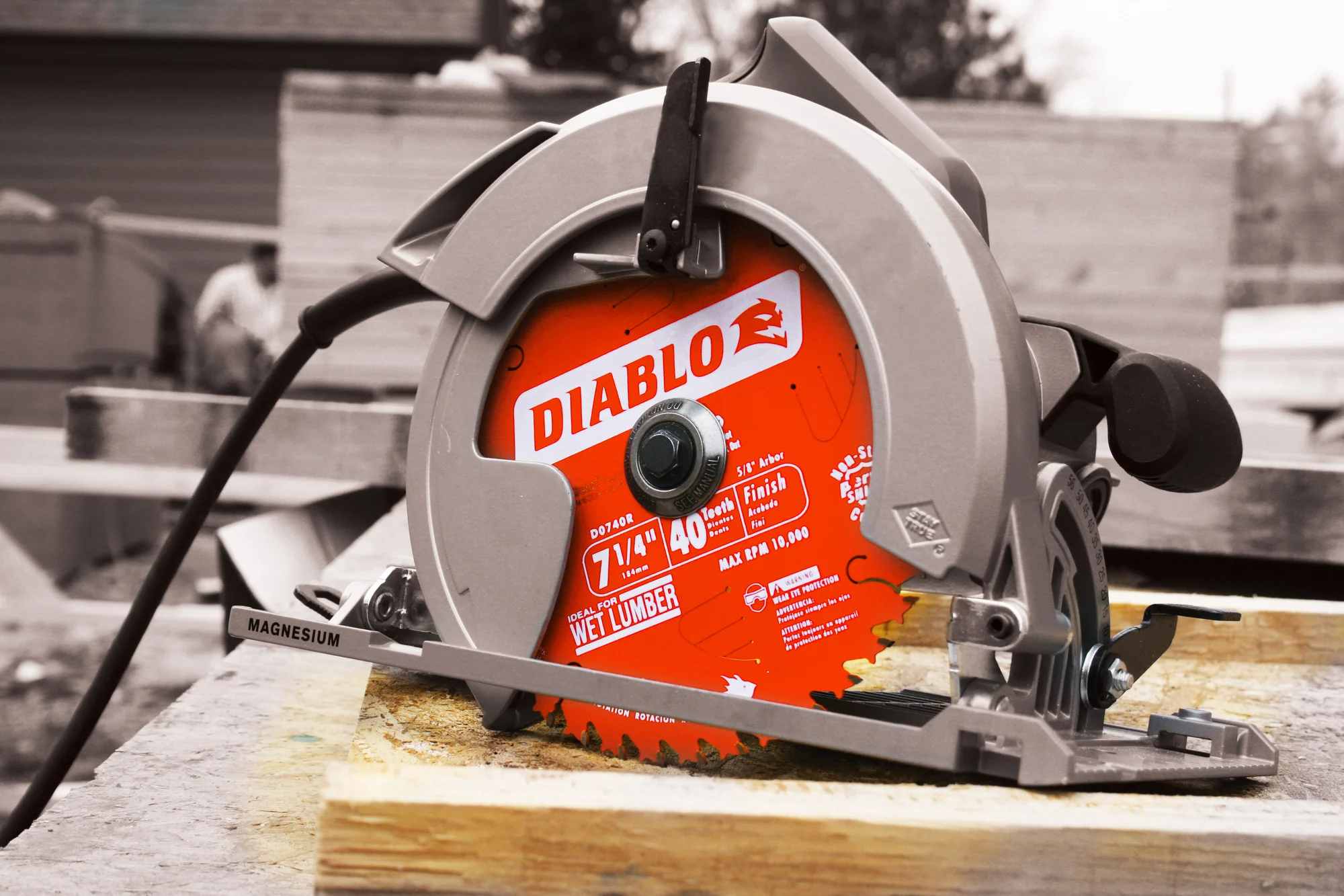 A close-up outdoor jobsite application photo showing a red Diablo 7-1/4 inch 40T circular saw blade fully mounted inside a grey magnesium corded circular framing saw, which is resting on a wood lumber plank at a residential construction site.