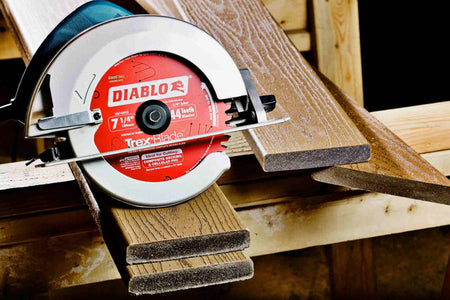 Action shot of a professional circular saw equipped with a Diablo D0744CD TrexBlade performing a clean, burr-free cut on a piece of brown composite decking material at a construction site.