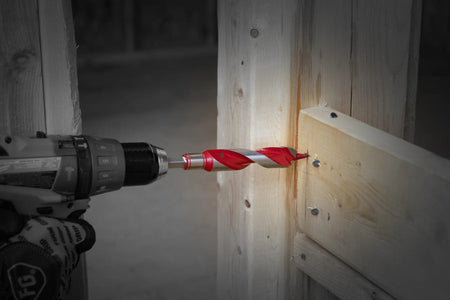 Close-up action shot of the Diablo 7/8-inch auger bit attached to a cordless drill, efficiently boring a hole through a structural wood header on a construction job site.