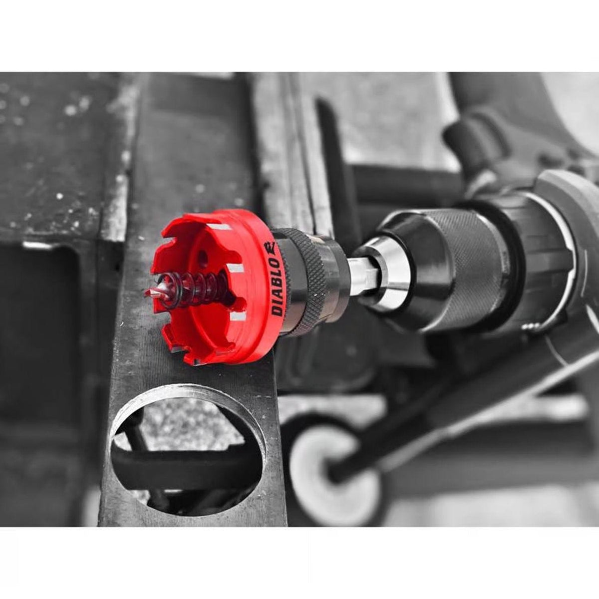 A high-action photograph showing a Diablo hole saw with a spring-loaded pilot bit attached to a handheld drill, positioned against a metal structural beam.