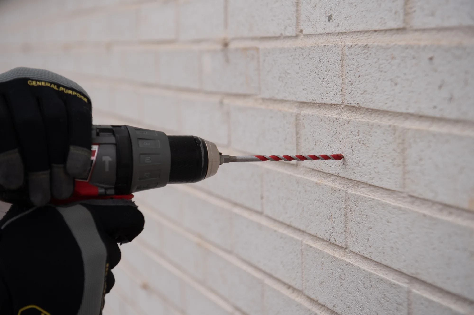 Action shot of a professional using a cordless hammer drill with the Diablo DMARG1180 carbide-tipped bit to bore a precise hole into a white brick masonry wall.
