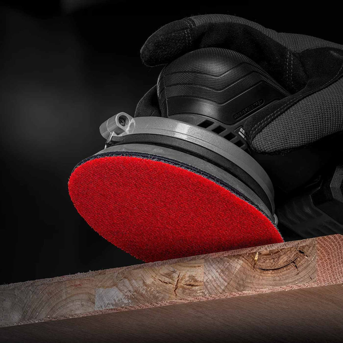 Close-up of a professional orbital sander equipped with a Diablo Sand Demon ceramic net disc performing aggressive material removal on the edge of a thick hardwood plank.