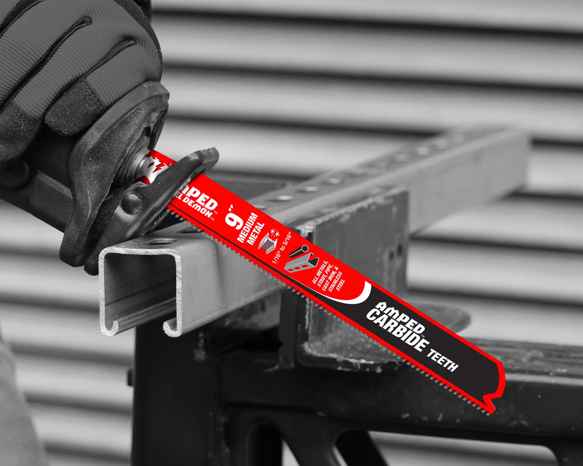 A close-up application photograph showing a gloved technician using a reciprocating saw equipped with a red Diablo AMPED medium metal carbide blade to cut straight down through a solid galvanized steel unistrut structural channel on a jobsite workbench.